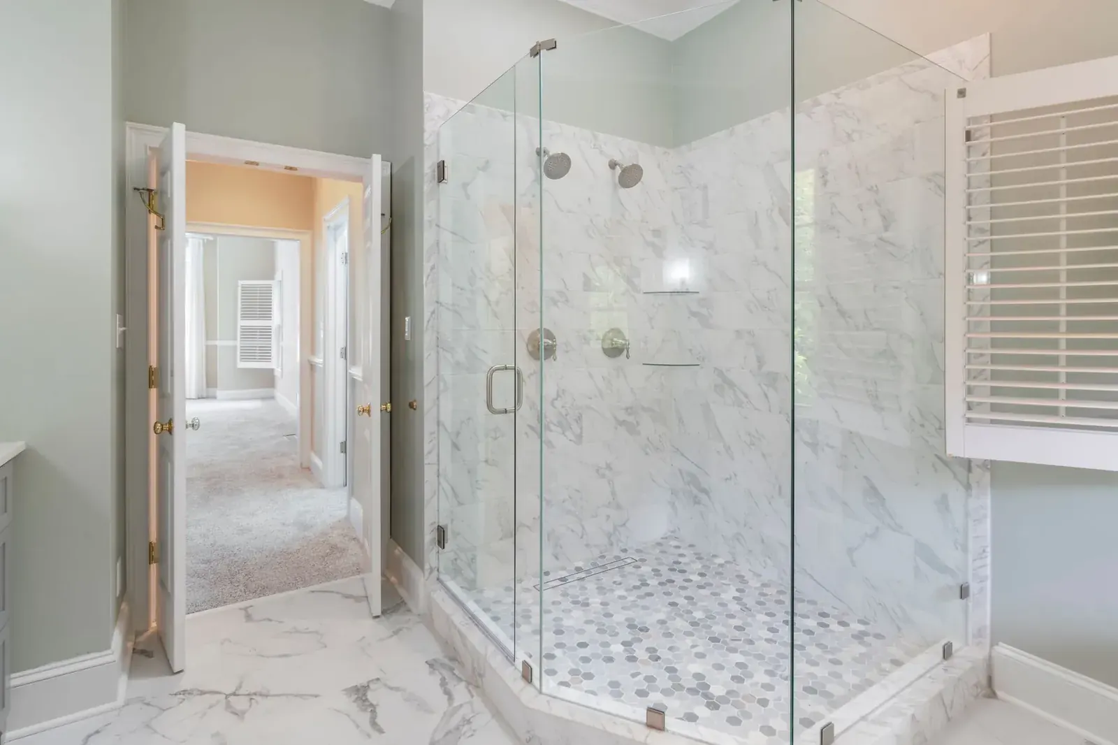 Frameless glass walk-in shower with marble-look tile and pebble floor